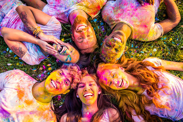 A group of friends lying down on the grass as they are filled with the Holi colours